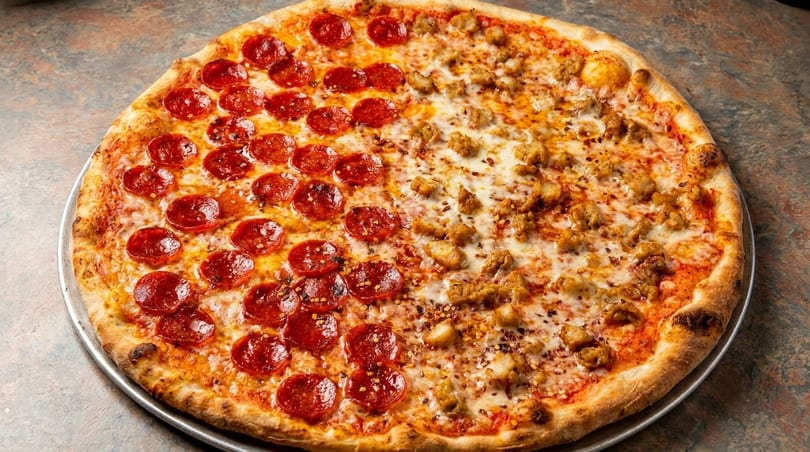 A large half pepperoni, half sausage pizza on a metal tray, with a rustic countertop background.